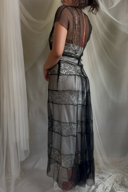 Woman wearing a long, elegant 1930s dress with intricate detailing against a white curtain backdrop.