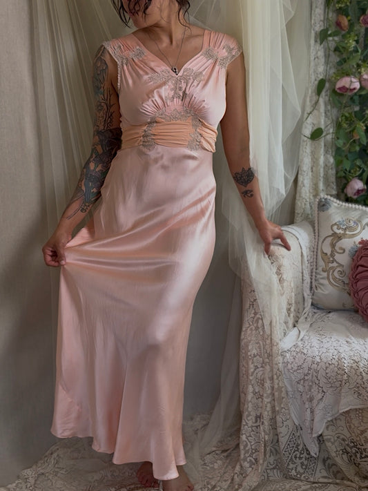 Woman wearing a vintage 1930s 1940s  pink silk bridal nightgown in a softly lit room with decorative elements.